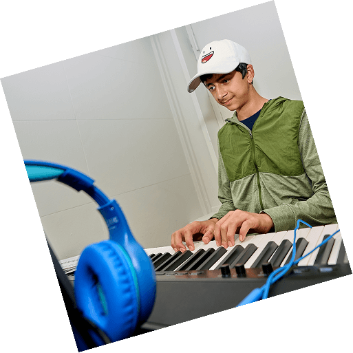 A teen smiles as he plays a melody on a digital keyboard in a bright piano studio