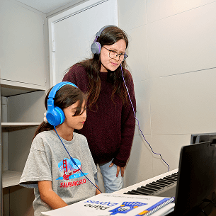 A teacher and child both look at their music book smiling during a piano lesson.