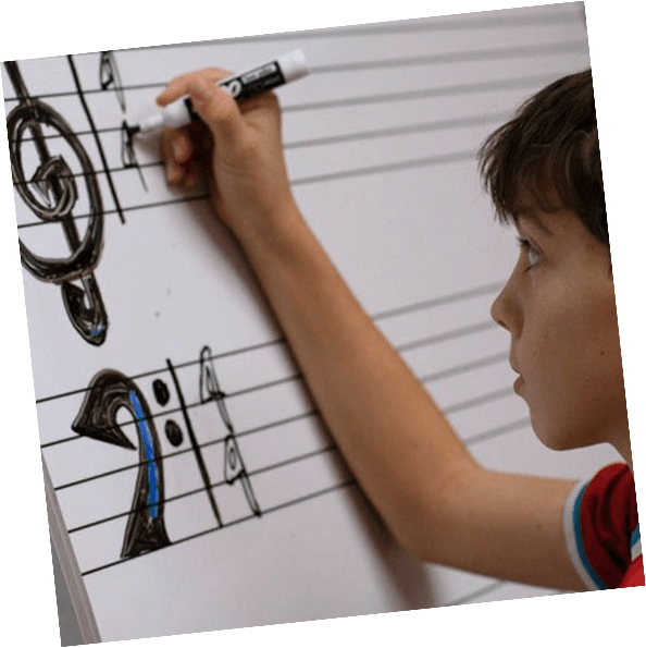 A boy writes on a whiteboard as he learns about music theory during a beginner kids piano class.