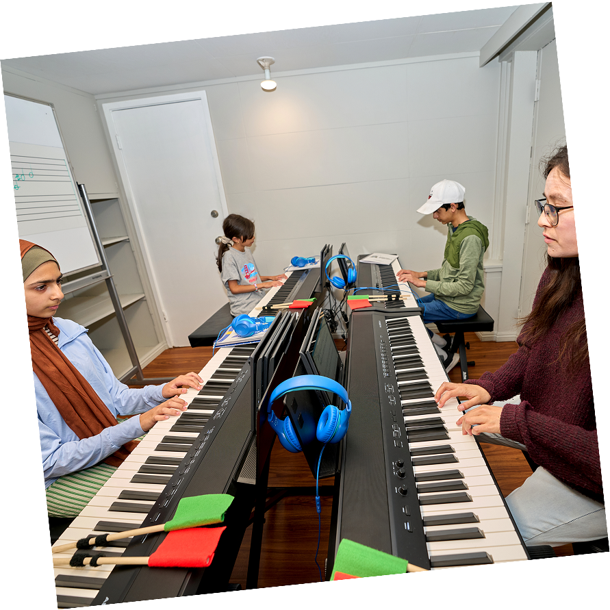 Teacher leading a group piano class with three children playing together.